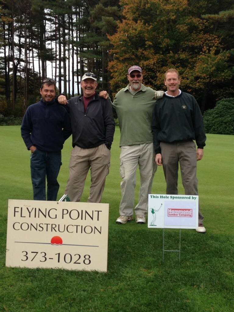 Four men standing on a golf course with a sign.