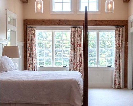 A bedroom with two large windows and a bed.