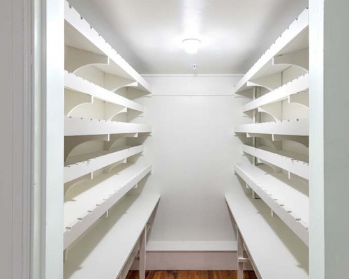 A white pantry with shelves and lights in it.