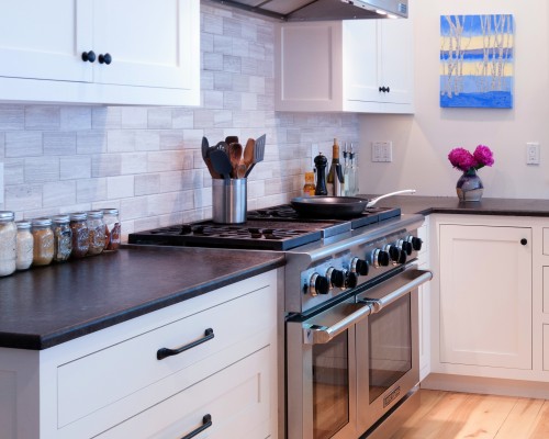 A kitchen with white cabinets and black counter tops.