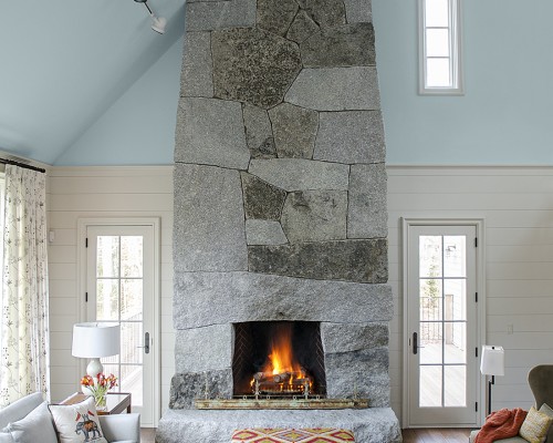 A living room with a stone fireplace and two windows.