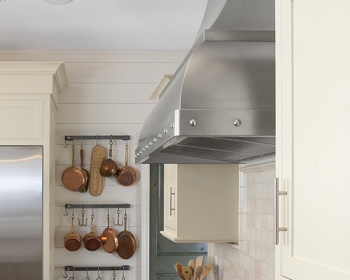 A kitchen with white cabinets and copper pots hanging on the wall.