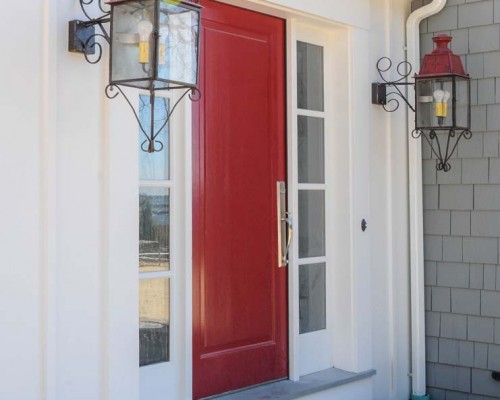 A red door and two lights on the side of a house.