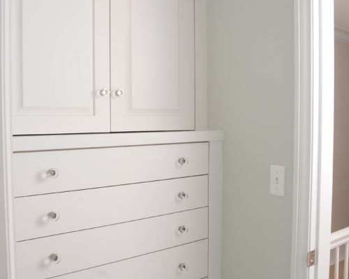 A white cabinet with drawers and doors in the corner of a room.