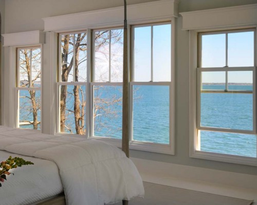 A bedroom with two large windows overlooking the water.