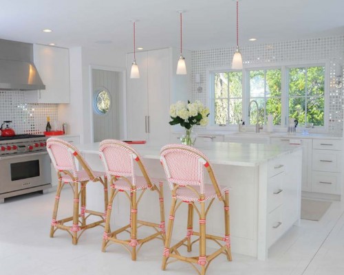 A kitchen with three pink chairs and white counters.